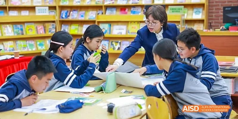 Students and a teacher collaborating around a table with laptops and other materials at Beijing 21st Century School.