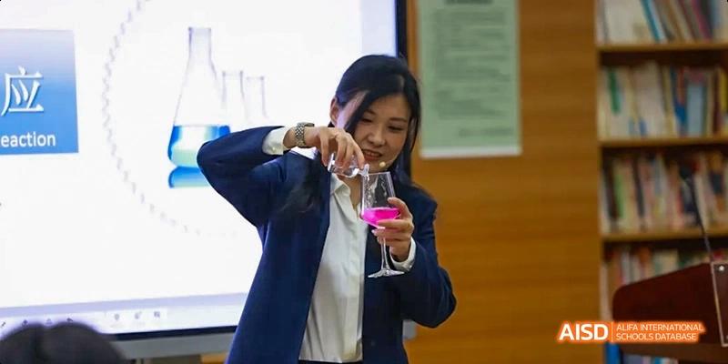A teacher conducting a science experiment, pouring liquid from one beaker to another, in a classroom setting at Beijing 21st