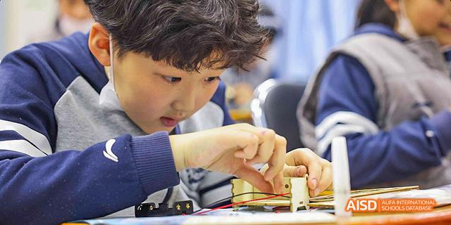 A student carefully building a small structure with wooden blocks at Beijing 21st Century School.