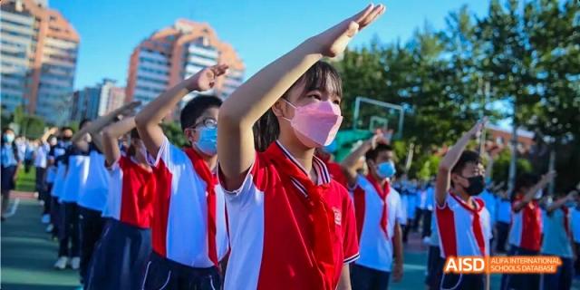 A female student with her arms raised in excitement outdoors at Beijing 21st Century School.