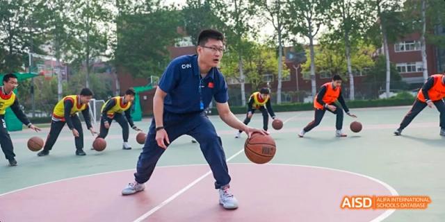 A teacher dribbling a basketball during a sports event at Beijing 21st Century School.