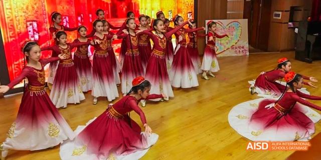 Students performing a traditional dance in red costumes on a stage at Beijing 21st Century School.