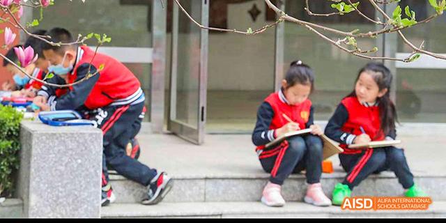 A female student in a red jacket sitting on steps outdoors at Beijing 21st Century School.