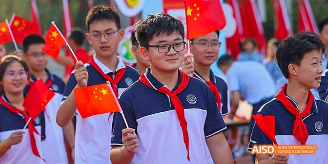 Students smiling while holding small Chinese flags at Beijing 21st Century School.