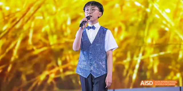 A male student singing into a microphone on stage at Beijing 21st Century School.