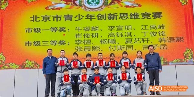 A group of students and teachers standing for a group photo in front of a banner at Beijing 21st Century School.