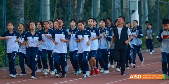 A group of students and a teacher cheering in a hallway at Beijing 21st Century School.