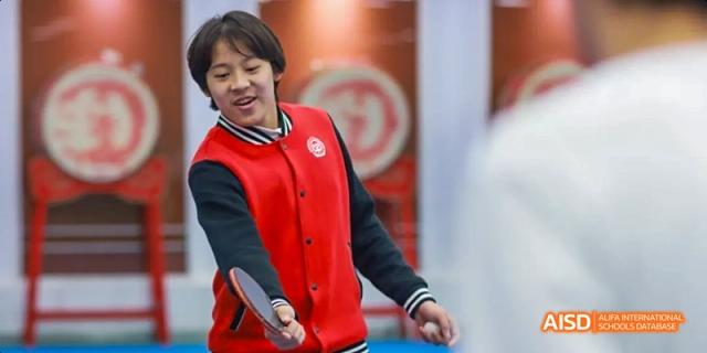 A female student in a red vest is smiling while looking at the camera at Beijing 21st Century School.