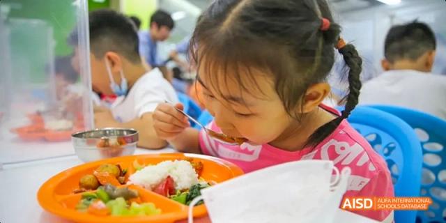 A young girl eating a meal from a plate at Beijing 21st Century School.