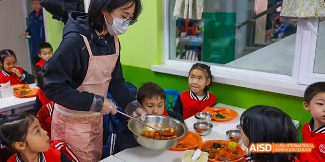A teacher helping a young student eat their meal in the cafeteria at Beijing 21st Century School.
