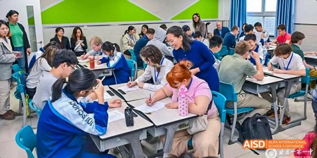 Students are seated at a table, looking at a book and a laptop at Beijing 101 Middle School.