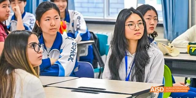 A female student is seated at a desk, smiling at the camera at Beijing 101 Middle School.
