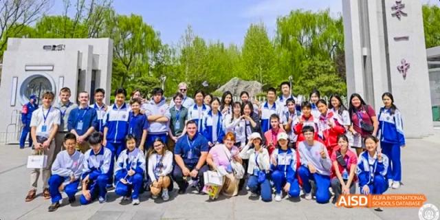 A large group of students are posing for a group photo outdoors on a grassy area at Beijing 101 Middle School.