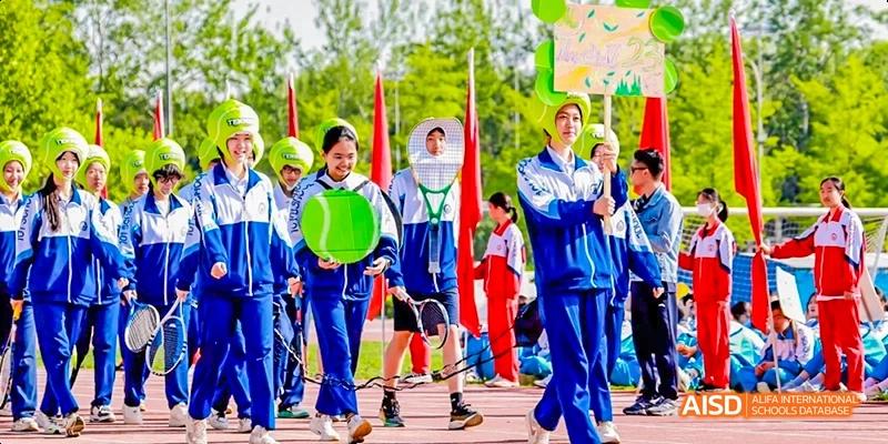 A group of students in blue and red uniforms are standing and holding a green banner at an outdoor event at Beijing 101 Middle School.