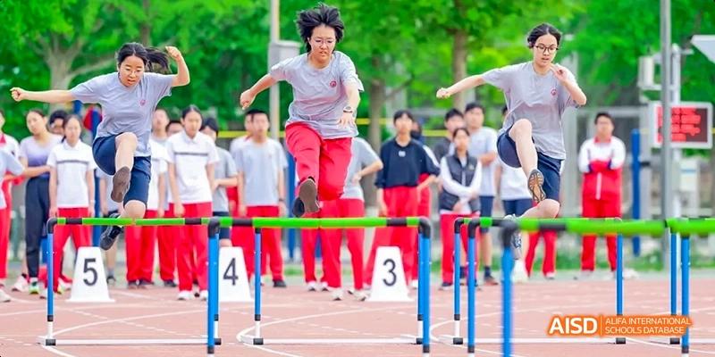 A female teacher is jumping over a hurdle on a sports track during an event at Beijing 101 Middle School.
