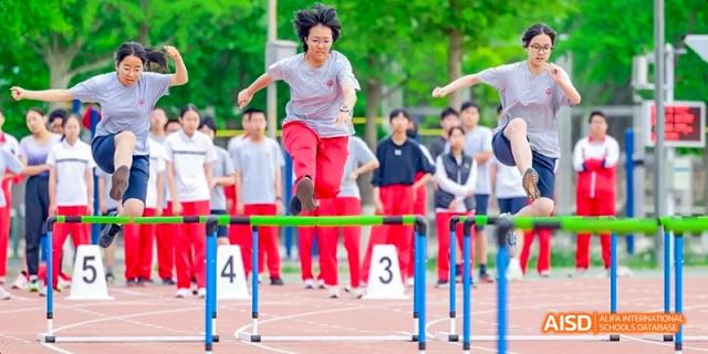 A female teacher is jumping over a hurdle on a sports track during an event at Beijing 101 Middle School.