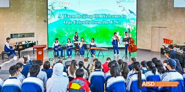 A large group of students is seated in an audience, watching a presentation on a stage at Beijing 101 Middle School.