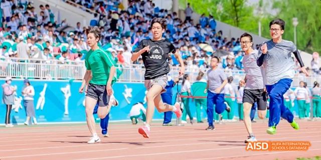 A female student in a green shirt is kicking a soccer ball on a sports field while others watch at Beijing 101 Middle School.
