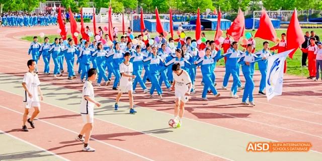 A large group of students in blue and red uniforms are gathered on a sports field for an event at Beijing 101 Middle School.