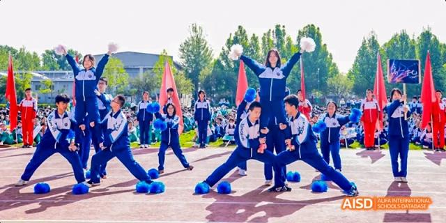 A group of students in blue and white uniforms are posing for a group photo on a sports field, with two holding a large flag at Beijing 101 Middle School.