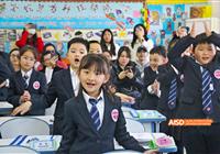 Beijing Bacui Bilingual School A young student in a school uniform smiles at the camera while in a classroom with other students.