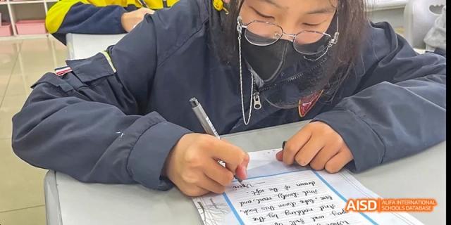 Beijing Bacui Bilingual School A close-up of a student in a blue uniform writing on a piece of paper.