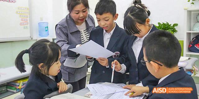 Beijing Bacui Bilingual School Students and a teacher or adult collaborate and look over papers at a table.
