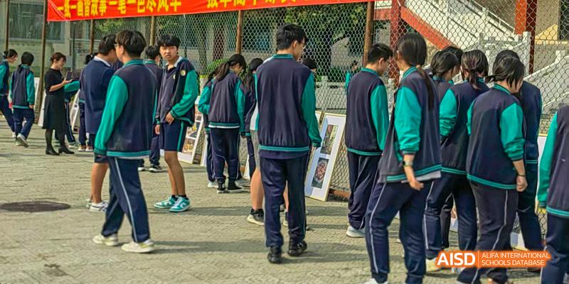 Beijing Bacui Bilingual School A group of students in dark blue and green school uniforms standing outdoors.