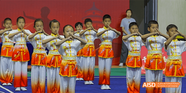 Beijing Bacui Bilingual School Young children in traditional white and orange uniforms performing a choreographed routine indoors.