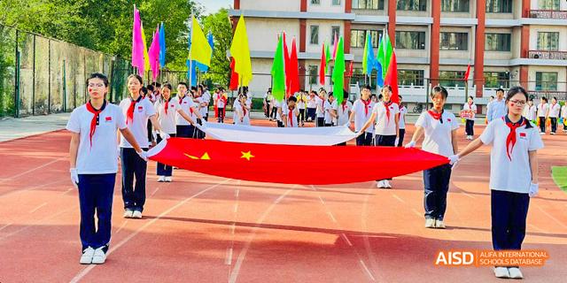 Beijing Bacui Bilingual School A group of students carrying a large Chinese flag and other colorful flags on a running track during an event.