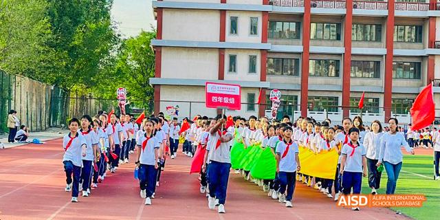 Beijing Bacui Bilingual School Students parading in a line, holding green and yellow flags with a school building in the background.