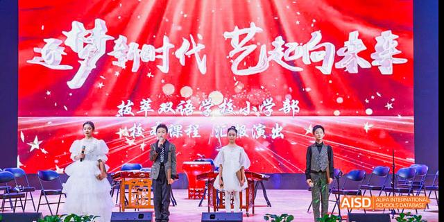 Beijing Bacui Bilingual School Performers on an indoor stage with a red backdrop and Chinese characters, one person playing a large drum.