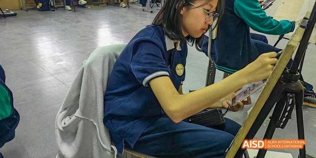Beijing Bacui Bilingual School A female student wearing a blue school uniform sits at a desk and focuses intently on her work.