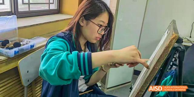 Beijing Bacui Bilingual School A female student wearing glasses and a blue and green uniform is focused on an art project.