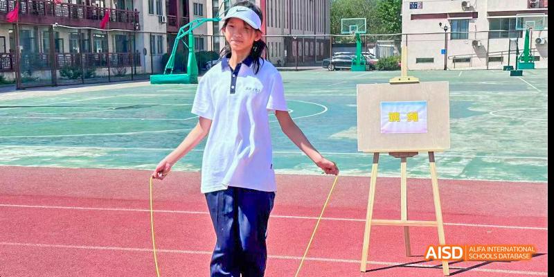 Beijing Bacui Bilingual School A student in a white shirt and blue pants stands on a running track, holding jump ropes.