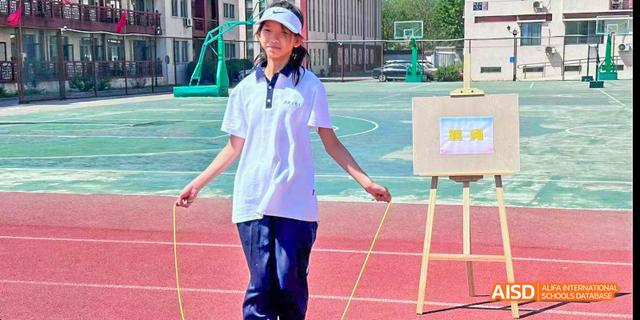 Beijing Bacui Bilingual School A student in a white shirt and blue pants stands on a running track, holding jump ropes.