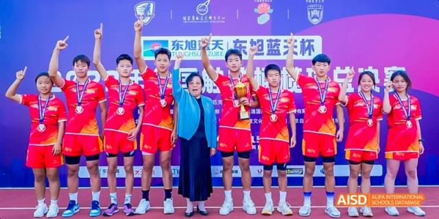 Beijing Bacui Bilingual School A winning team of students in red uniforms holds medals and a trophy with an adult.
