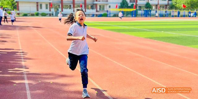 Beijing Bacui Bilingual School A young student with pigtails runs on a running track with a determined expression.