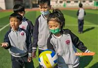 Beijing Bacui Bilingual School Two students play with a yellow volleyball, one of them wearing a mask.