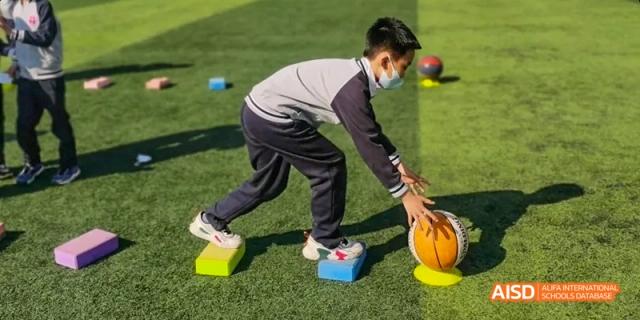 Beijing Bacui Bilingual School A student wearing a mask leans down to hit a ball with their head on a sports field.