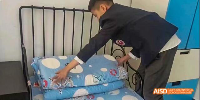 Beijing Bacui Bilingual School A male student in a blazer makes his bed in a dorm room.