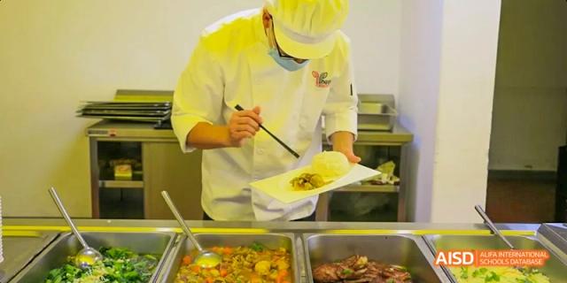 A photo showing a man in a cafeteria serving food to students, at Beijing Enlighten School.