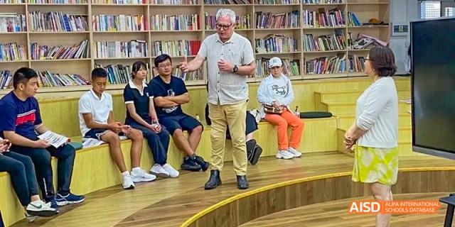 A photo showing an old man teaching a group of students in a library, at Beijing Enlighten School.