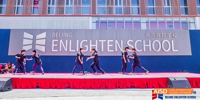 A photo showing students performing on a stage, with the text "ENLIGHTEN SCHOO" in the background, at Beijing Enlighten School.