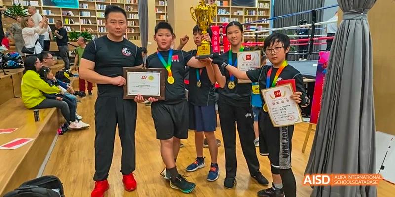 A photo showing a group of students posing for a photo with trophies and medals, at Beijing Enlighten School.