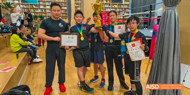 A photo showing a group of students posing for a photo with trophies and medals, at Beijing Enlighten School.