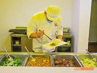 A photo showing a man in a cafeteria serving food to students, at Beijing Enlighten School.