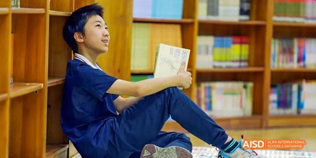A male student from Beijing Haidian Foreign Language Academy sitting on the floor and reading a book in the school library.
