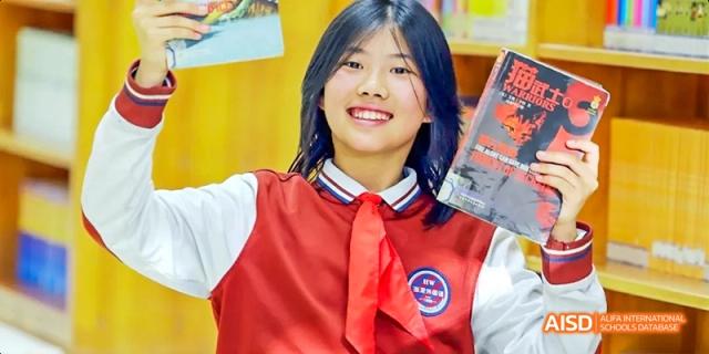 A female student from Beijing Haidian Foreign Language Academy smiling while holding a book in the school library.