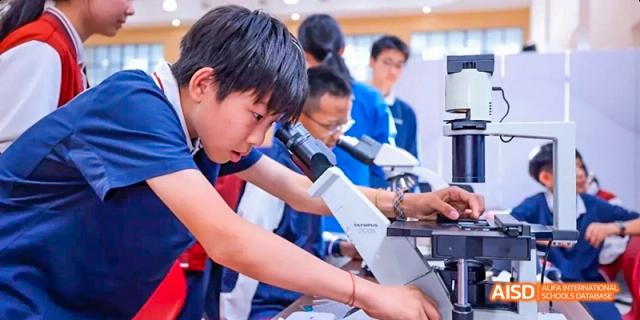 A male student from Beijing Haidian Foreign Language Academy using a microscope in a science lab.